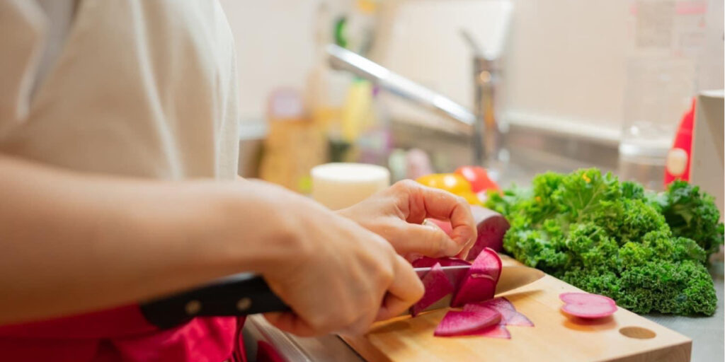 健康料理家の調理風景。ビーツを薄くスライスし、ケールなどの野菜を使った健康的なメニューを準備する手元。