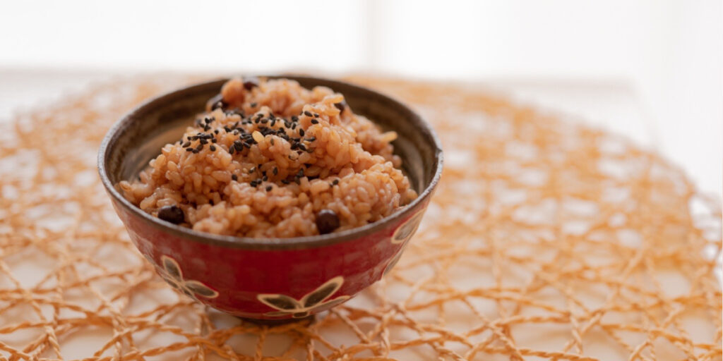 赤い器に盛られたお赤飯。健康料理家が紹介する、小豆と黒ごまを使った体に優しい和食メニュー。